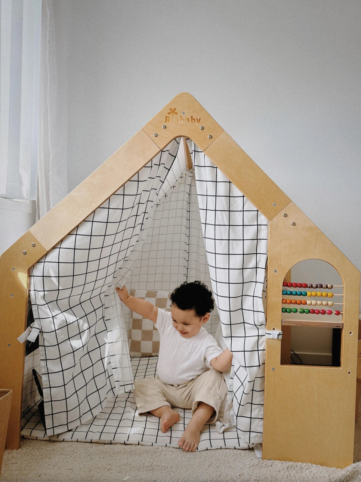 A child peeking through the curtains of a Riababy wooden cubby house