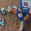 Toy set with space-themed items including a rocket, spaceship, and astronaut figure on a sandy surface.