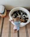 Child playing with colorful balls in a white ball pit on a patterned floor.