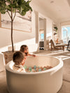 Two children playing with colorful balls in a white ball pit in a modern living room.